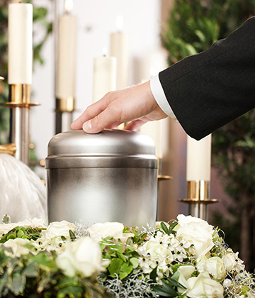 Hand resting on a funeral urn surrounded by white flowers